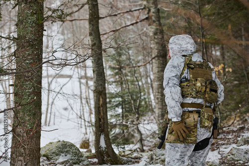 Fotografie Soldier In White Winter Camouflage Patrols Snowy Forest With Tactical Gear, Back