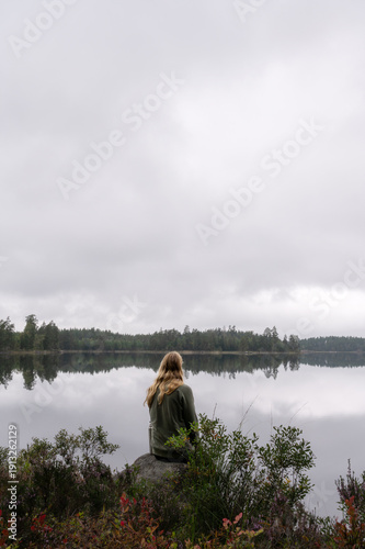 Fotografie Person sitting by calm forest lake under overcast sky