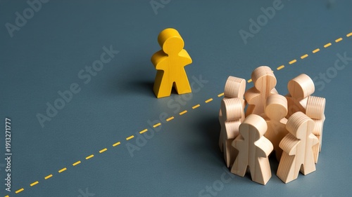 A yellow wooden figure stands alone, separated by a dashed line from a group of natural wooden figures, symbolizing isolation or individuality.