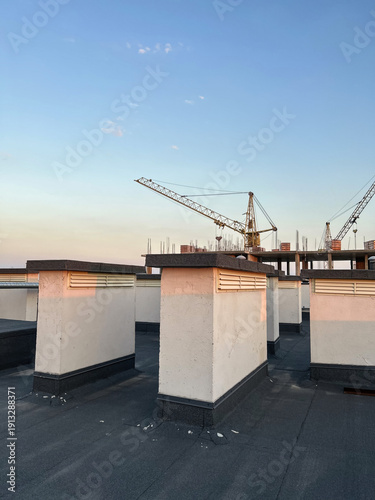 Construction site featuring cranes and ventilation shafts on rooftop during evening, showcasing urban development and architectural elements