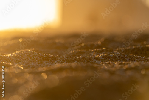 Golden sunset light reflecting over wet sand, capturing delicate textures and shimmering highlights in a calm, minimal coastal scene.