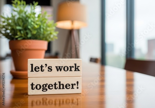 Wooden blocks stacked with text lets work together on table. Indoor office scene with plant and blurred background. Concept for cooperation and teamwork.