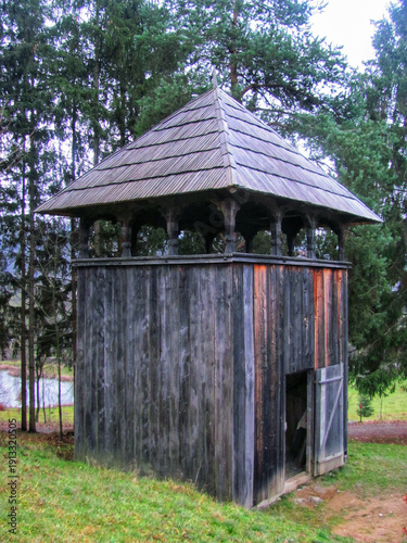 Traditional wooden bell tower structure with a pyramid roof located in a scenic countryside forest