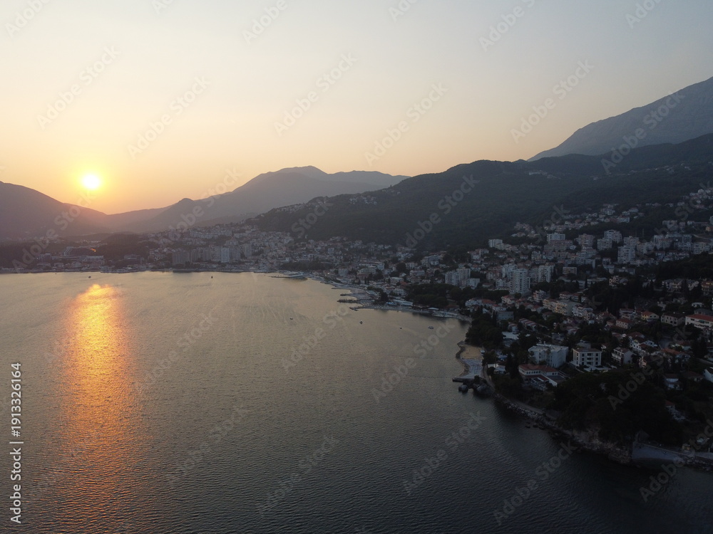 Fototapeta premium Coastal City at Sunset: Tranquil Waters and Mountain Backdrop Scenery