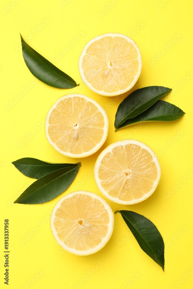 Fototapeta premium Pieces of ripe lemons and leaves on yellow background, flat lay