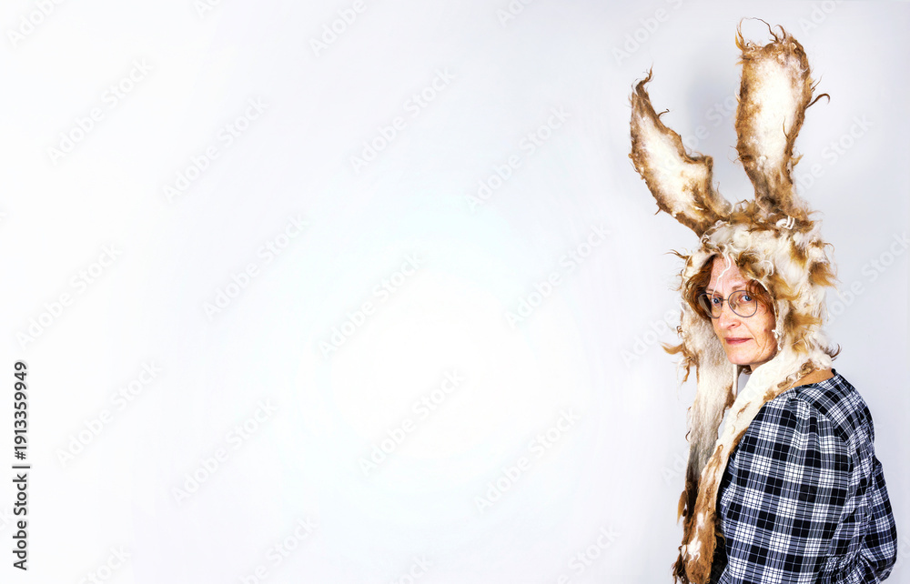 Fototapeta premium Woman wearing felted wool bunny hat with long ears standing against a white wall with copy space