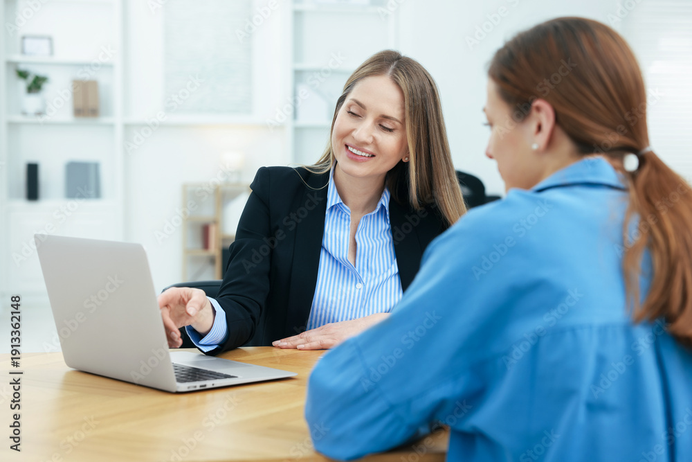 Obraz premium Smiling recruiter showing something on laptop to candidate during job interview at table in office