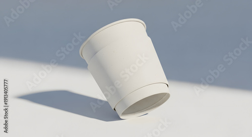 White disposable paper coffee cup, tilted, casting a shadow on a bright white background.