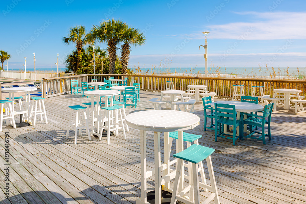 Fototapeta premium An empty beachfront cafe patio with palm trees along the sea grass and sand dunes of the Atlantic Ocean Grand Strand, at North Myrtle Beach, South Carolina.