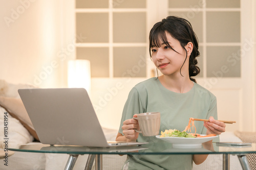 Foto Young Asian woman relaxing and looking at laptop while eating at home in the eve