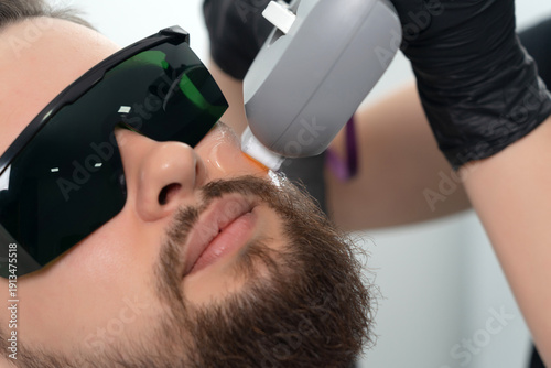 Φωτογραφία Young bearded man getting laser facial treatment by professional cosmetologist in a beauty clinic