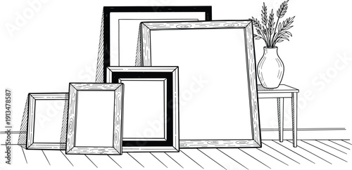 Collection of empty picture frames of various sizes and styles arranged on a wooden floor next to a vase of dried plants on a stool