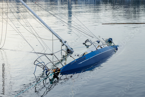 Foto Sunken blue sailboat partially submerged in calm water with tilted hull, mast, a