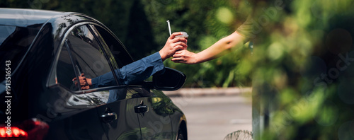 Hand Man in car receiving coffee in drive thru fast food restaurant. Staff serving takeaway order for driver in delivery window. Drive through and takeaway for buy fast food for protect covid19.