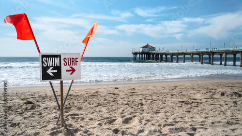 Red warning flags and a posted sign indicating areas for swimming and surfing during hazardous conditions at Manhattan Beach, California, USA.