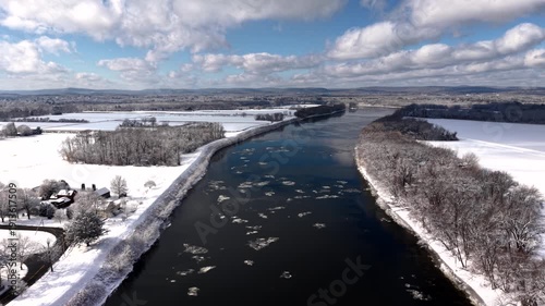 Wallpaper Mural Aerial view of winding river with floating ice, surrounded by snow covered fields and trees under bright winter sun in rural America. Wide shot. Torontodigital.ca