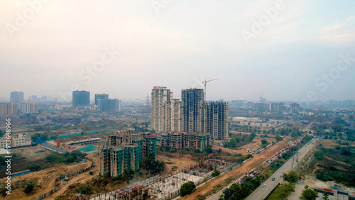 drone view of high-rise residential buildings under construction with crane in Gurgaon with hazy skyline, highlighting urban growth, real estate development, and air pollution.
