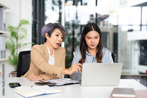Billede på lærred Confident mature business professional woman talking to younger female colleague at office table, speaking, gesturing, teaching, explaining work tasks