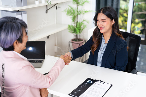 employer hr with employment contract job on desk officer hiring welcoming female asian newcomer worker manager shaking hands in contemporary office. Getting new job handshake concept.