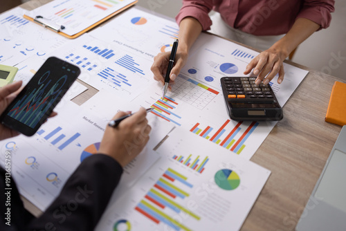 Top view of business people analyzing marketing reports, financial charts, and sales performance using calculators and pens in a meeting room.