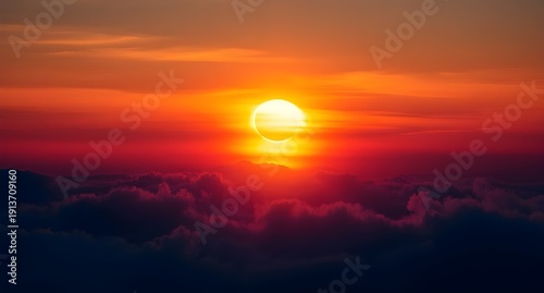 Bright sun sinks below the horizon above dense clouds below.
