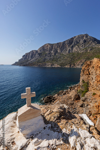 Small cross by the Aegean Sea on the rugged, rocky and mountainous island of Telendos in Greece on a sunny day.