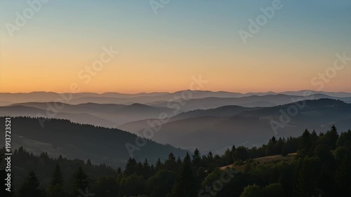 Hazy mountain layers at sunset, with foreground treeline and soft, warm light