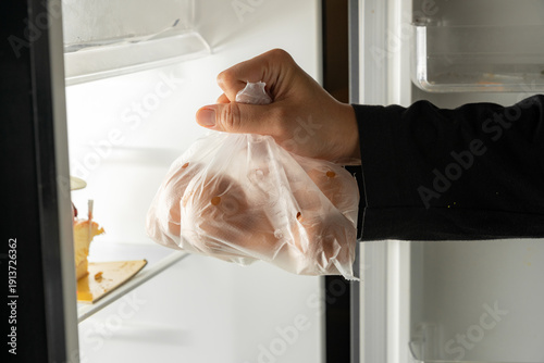 Hand placing a bag of fresh brown eggs into a refrigerator for storage at home