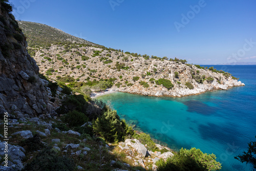 View of a small and idyllic beach in a cove surrounded by rugged and hilly coastline by the Aegean Sea on Kalymnos island in Greece on a sunny day.
