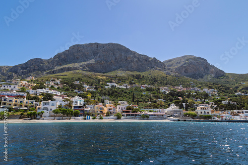 Mountains and lush hill behind the buildings at the Mirties village by the Aegean Sea on Kalymnos island in Greece on a sunny day.
