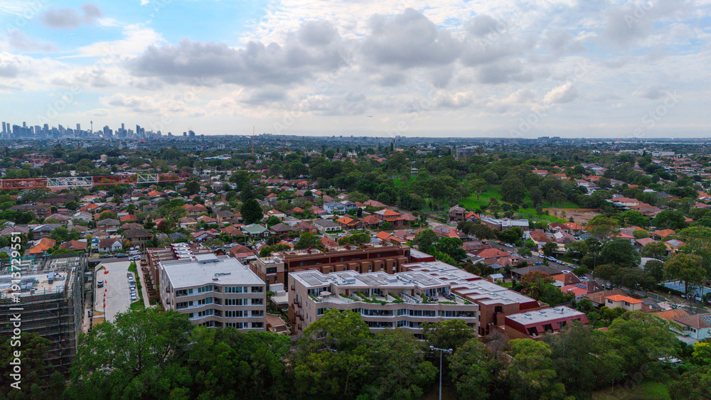 Fototapeta premium Panoramic Aerial Drone view of Inner Western Suburbs of Sydney housing, roof tops, the streets and the parks, the roads and trees of Ashbury Ashfield Burwood Summer Hill Canterbury and Campsie in Sydn