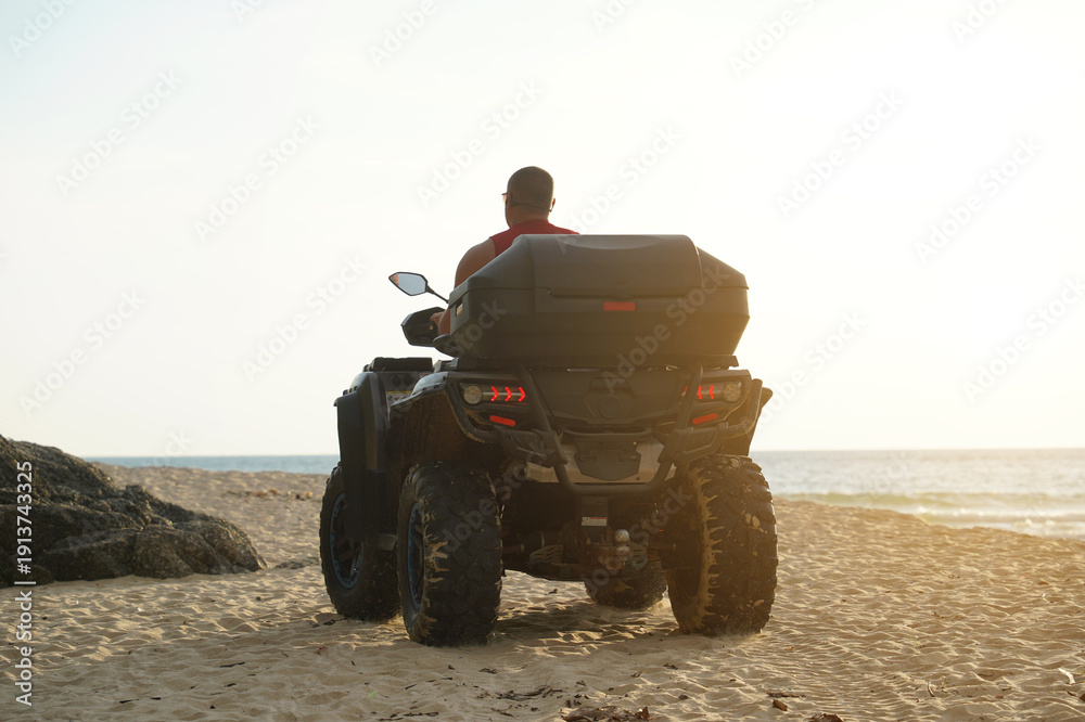 Fototapeta premium A man engages in extreme ATV riding on sand beach early in the morning