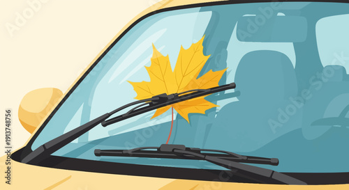 Yellow car windshield with a bright autumn leaf caught under wipers