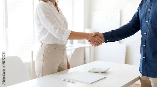 Two professionals finalize an agreement with a firm handshake across a desk, with calculator and documents present, signifying a successful business interaction.