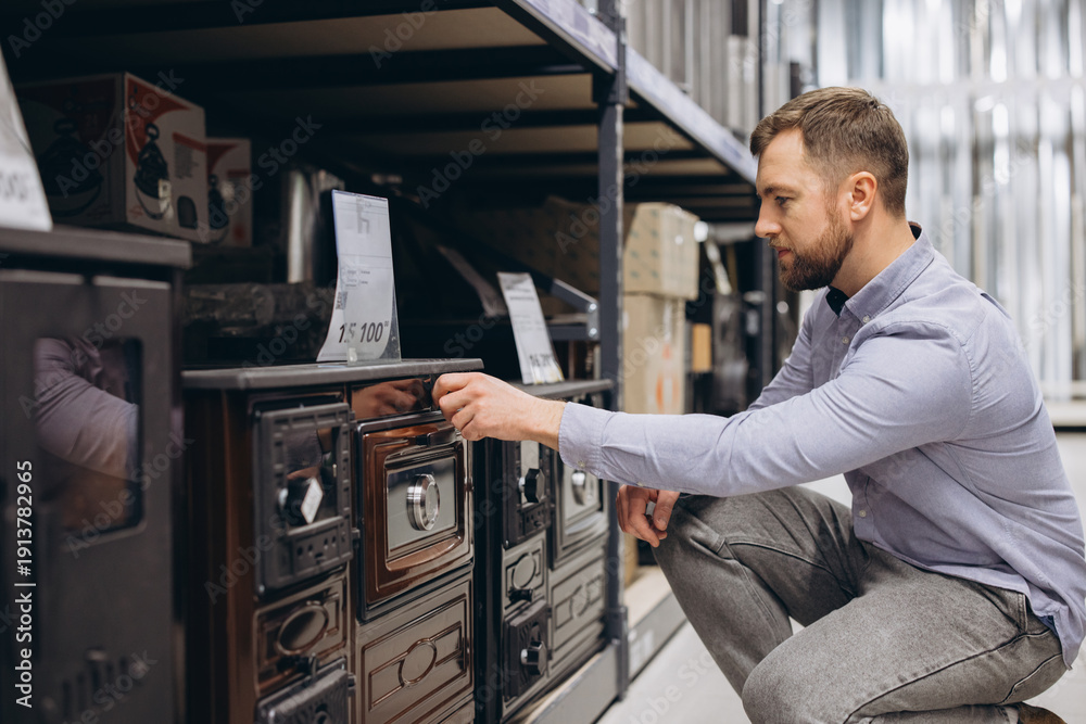Fototapeta premium Man examining a wood stove, browsing home heating equipment in a large retail store, making a purchase decision
