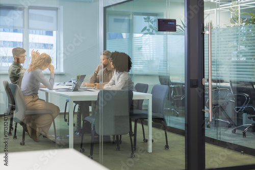 A view through a glass partition shows a modern, busy office interior. Job interview process is in office. Human resources, meeting and group of hiring candidates for vacancy.