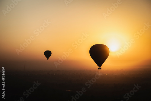 dos globos o balones aerostáticos volando por el cielo de Luxor en Egipto con el cielo ámbar del amanecer