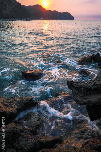 Ocean waves crashing on rocky shores at sunset, golden sunlight reflecting on sea surface, natural seascapes concept of freedom, peace, relaxation, travel, adventure, and nature beauty.