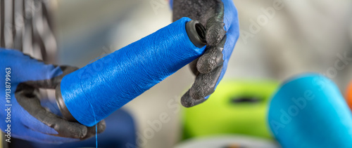 Foto Close up of worker hands in gloves holding blue yarn spool with colorful thread cones background in textile factory