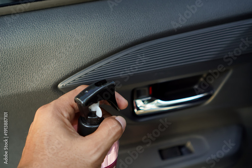 A woman’s hand sprays air freshener inside a car interior