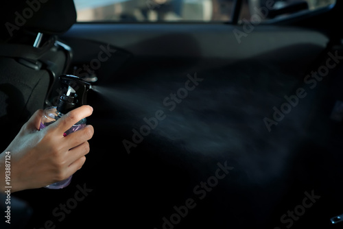 A woman’s hand sprays air freshener inside a car interior
