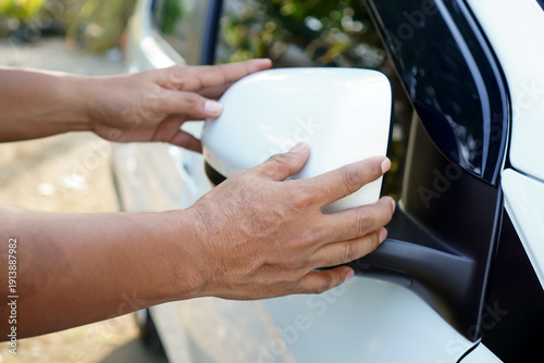 Close-up of a man's hand adjusting the side mirror of a white car outdoors