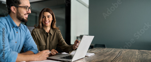 Happy busy female manager explaining corporate software work talking to young male employee consulting client working on computer using laptop discussing business project plan at office meeting.