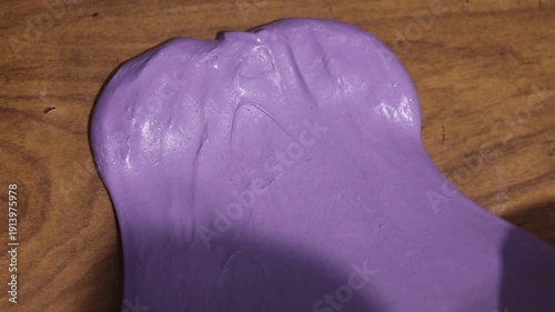 Children's hands knead a soft purple smiley face on a wooden table.
