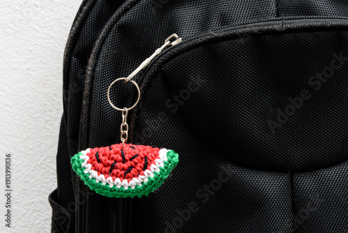 A plush keychain in the shape of a slice of watermelon that attaches to the zipper of a school backpack. Keychain handmade using the amigurumi crochet technique.