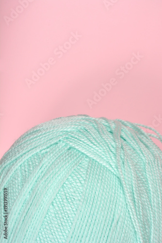 A ball of light mint green wool yarn placed on a solid pink surface with copy space