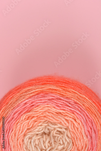 A round ball of gradient wool yarn transitioning from cream to orange sits on a solid pink background