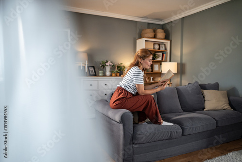 Canvastavla Young woman relaxing reading book at home in living room