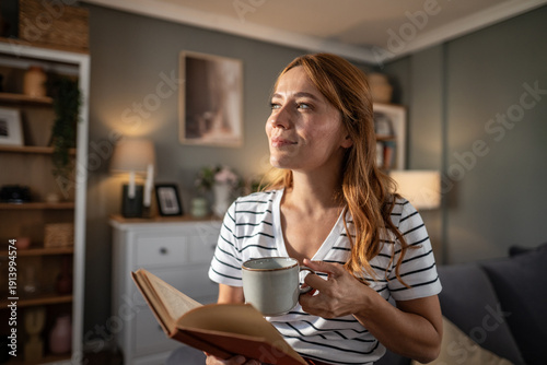 Woman relaxing at home reading book holding coffee mug