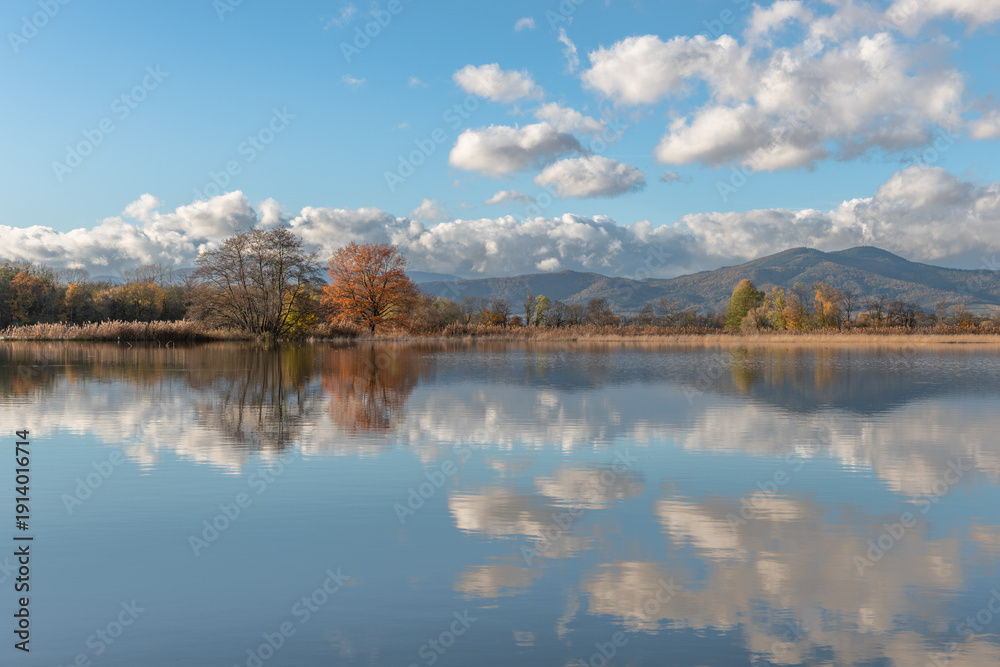 Fototapeta premium River with clouds and mountains under blue sky floods plain in autumn